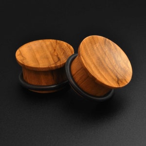 May include: Two wooden ear gauges with a brown wood grain pattern and black rubber o-rings.