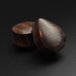 May include: Two wooden ear gauges, one round and one teardrop shaped, with a dark brown wood grain.