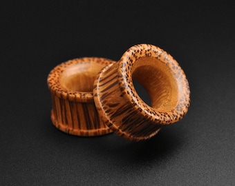 May include: Two wooden ear gauges with a striped pattern. The gauges are brown and have a natural wood finish.