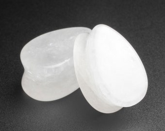 Puede incluir: Dos medidores de oreja de piedra blanca, con forma de lágrima, sobre un fondo negro.