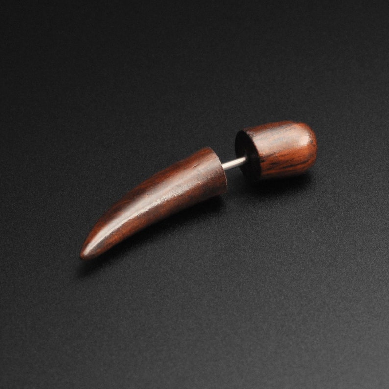 May include: A single, dark brown wooden earring with a tapered, horn-like design. The earring has a cylindrical post and a rounded back. The earring is set against a black background.
