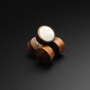 May include: Three wooden ear gauges with a white mother of pearl inlay. The gauges are stacked on top of each other.