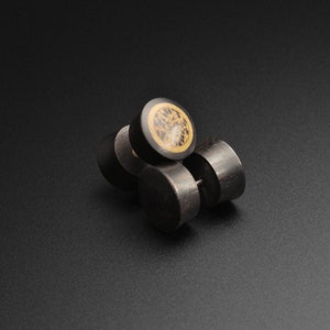 May include: Three black wooden ear gauges with a gold and black patterned design.