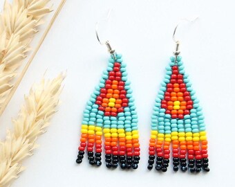 May include: A pair of turquoise, red, orange and yellow beaded dangle earrings with black fringe. The earrings are on a white background.