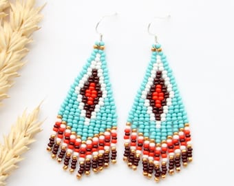 May include: A pair of turquoise, white, red and brown beaded dangle earrings with a geometric pattern. The earrings have silver hooks.