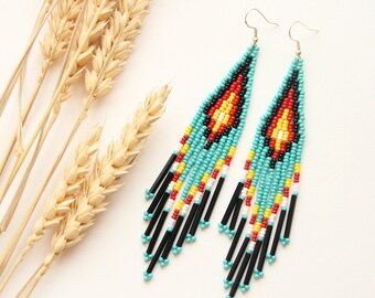 May include: A pair of long, beaded earrings with a turquoise, black, red, white, and yellow geometric pattern. The earrings are hanging from silver hooks.