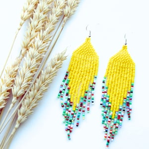 May include: A pair of long yellow beaded earrings with colourful accents. The earrings are made with small beads and have a fringe-like design.