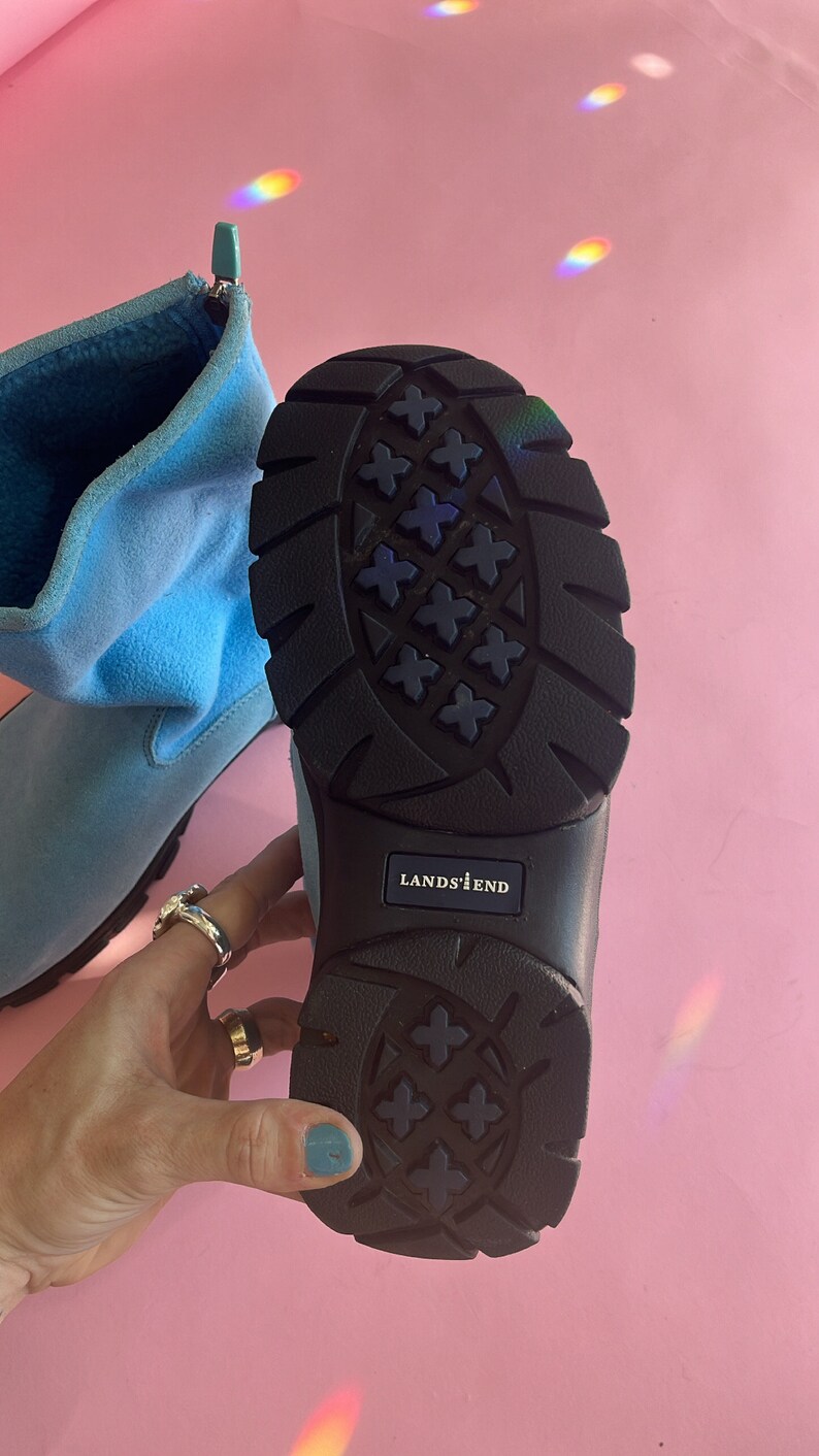 May include: Light blue Lands' End boot with a black sole. The sole has a textured pattern. The boot is made of a soft material and has a zipper. The Lands' End logo is visible on the sole.
