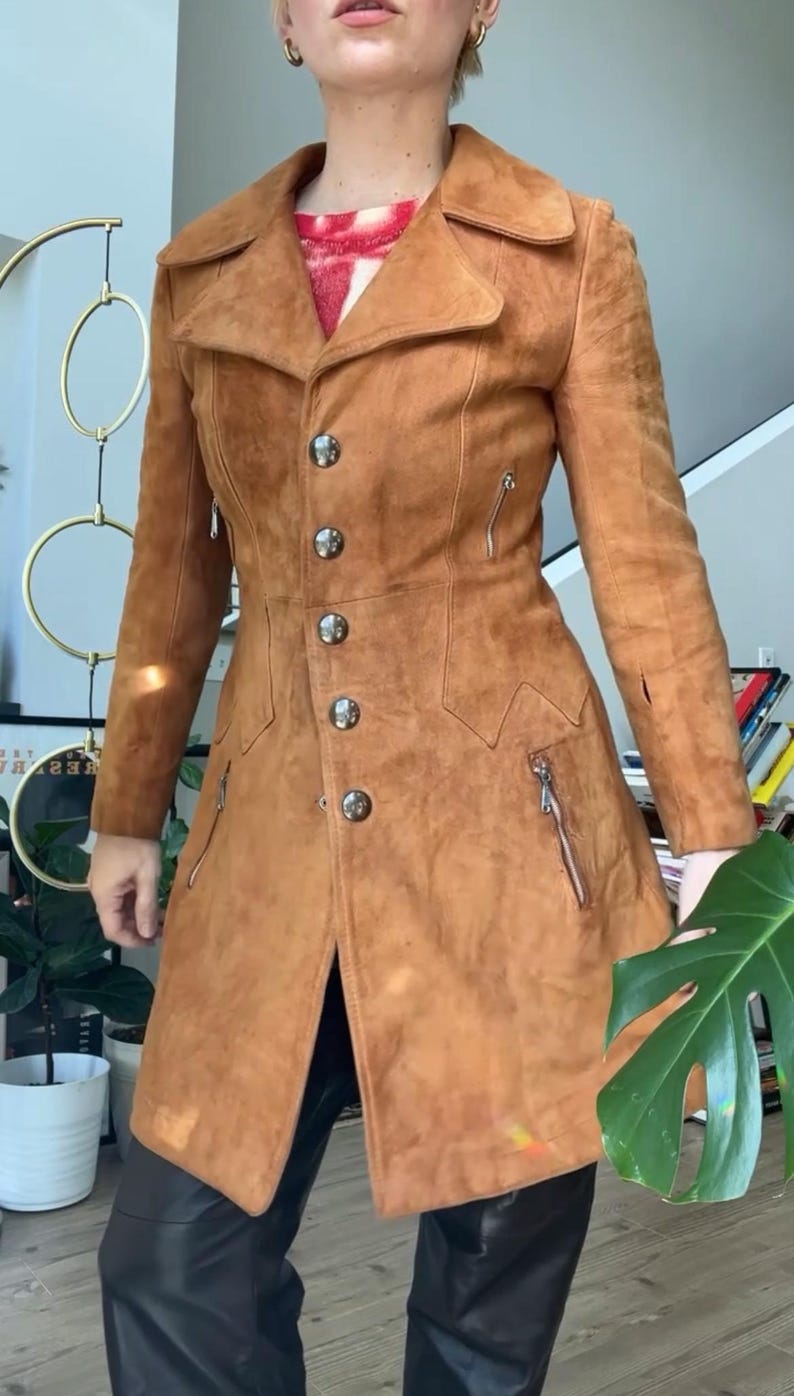 Peut inclure: Un manteau en daim marron clair avec une coupe ajust&eacute;e, un col crant&eacute;, des boutons argent&eacute;s et des poches zipp&eacute;es. Le manteau a une esth&eacute;tique vintage et un design classique, adapt&eacute; &agrave; diverses occasions.