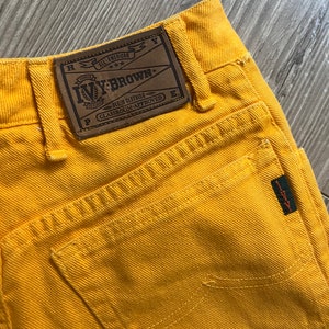 May include: Yellow denim pants with a brown leather patch that says "Ivy-Brown. All-American Denim Clothing. Classroom-Approved."
