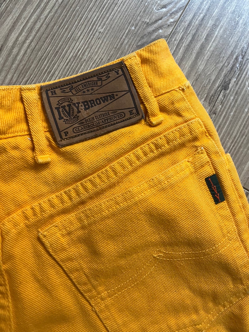 May include: Yellow denim pants with a brown leather patch that says "Ivy-Brown. All-American Denim Clothing. Classroom-Approved."