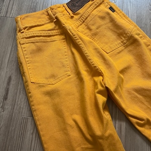 May include: A pair of yellow denim jeans with a brown leather patch on the back pocket that says "Lee" and "100% Cotton".