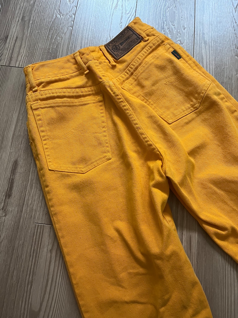 May include: A pair of yellow denim jeans with a brown leather patch on the back pocket that says "Lee" and "100% Cotton".