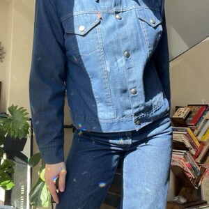 Op de afbeelding: Een spijkerjasje en bijpassende jeans in een medium blauwe wassing. De jas heeft een puntkraag, knoopsluitingen en twee borstzakken. De jeans is uitlopend. De outfit is casual en stijlvol.