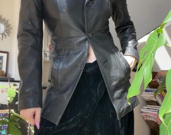 May include: A black leather blazer featuring a notched collar, long sleeves, and a three-button front closure. The jacket is tailored with a fitted waist and includes two side pockets. It is paired with black velvet wide-leg trousers.