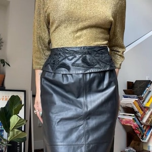 May include: A black leather skirt with a decorative black embroidered waistband. The skirt is paired with a gold sparkly top.