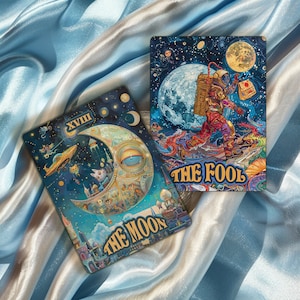 May include: Two tarot cards, The Moon and The Fool, with colourful illustrations and gold accents. The Moon card features a crescent moon with a large eye, a cityscape, and stars. The Fool card shows a figure in a spacesuit walking on a planet with a large moon in the background.