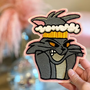 May include: A gray embroidered iron-on patch of Tom from Tom and Jerry wearing a pink and yellow ice cream cone hat.