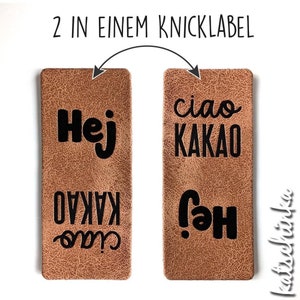 Può includere: Due etichette in pelle marrone con testo nero. La prima etichetta dice "Hej Kakao" e la seconda etichetta dice "ciao Kakao". Le etichette sono reversibili, quindi puoi usare entrambi i lati.