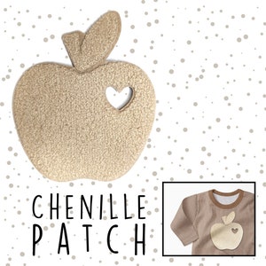 Könnte beinhalten: Ein beigefarbener Chenille-Aufnäher in Apfelform mit einem ausgeschnittenen Herzen. Der Aufnäher trägt den Schriftzug "Chenille Patch" in schwarzer Schrift. Der Aufnäher ist auf einem braunen Langarmshirt abgebildet.