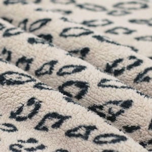 Könnte beinhalten: Nahaufnahme eines weichen, weißen Stoffes mit einem sich wiederholenden Muster aus dunkelblauen geometrischen Formen. Der Stoff hat eine flauschige Textur.
