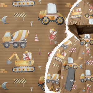 Op de afbeelding: Een bruin en geel kinderjack met een bouwthema. Het jack heeft een herhalend patroon van muizen die bouwvoertuigen besturen, waaronder een betonmixer, een bulldozer en een graafmachine. Het patroon bevat ook bouwtekeningen, bakstenen en gereedschap.