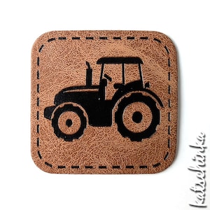 Puede incluir: Un parche de cuero marrón con una silueta negra de un tractor. El parche tiene un borde cosido.