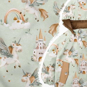 Op de afbeelding: Een groene stof met een herhalend patroon van witte eenhoorns met vleugels, regenbogen, wolken en kastelen. De stof wordt gebruikt om een ​​geklede jas met bruine bies te maken.