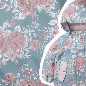 Puede incluir: Una chaqueta azul claro con capucha y un estampado floral con rosas rosas y hojas blancas. La chaqueta tiene dos bolsillos con forro de tela rosa y botones plateados.