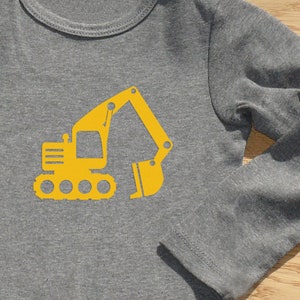 Puede incluir: Una camiseta gris de manga larga con una silueta amarilla de una excavadora en la parte delantera.