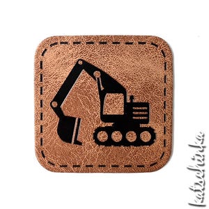Könnte beinhalten: Ein braunes Leder-Patch mit einer schwarzen Silhouette eines Baggers. Das Patch hat einen genähten Rand.