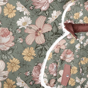 Könnte beinhalten: Eine grüne Kapuzenjacke mit einem Blumendruck mit rosa Rosen, gelben Gänseblümchen und weißen Hibiskusblüten. Die Jacke hat ein rotes Futter und zwei Taschen.