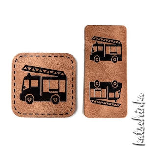 Könnte beinhalten: Zwei braune Leder-Patches mit schwarzen Umrissen von Feuerwehrautos. Die Feuerwehrautos haben Leitern und sind nach rechts ausgerichtet. Die Patches sind rechteckig und haben einen genähten Rand.