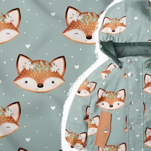 May include: A light blue hooded jacket with a repeating pattern of brown foxes wearing flower crowns on a white background. The jacket has brown accents on the pockets and zipper.