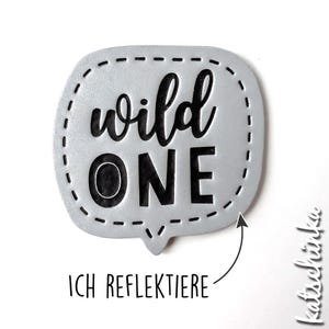 Op de afbeelding: Een zilverkleurige spraakballon met een zwarte gestikte rand en de tekst "wild one" erin. De spraakballon is een knutselvoorziening voor scrapbooking of kaartmaken.
