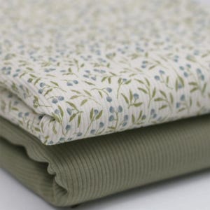 Könnte beinhalten: Zwei Stoffstücke, eines mit weißem Hintergrund und einem kleinen blauen Blumenmuster, das andere einfarbig in Salbeigrün. Beide Stoffe haben eine gerippte Textur.