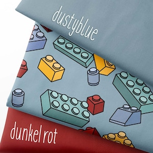 Könnte beinhalten: Drei Stoffmuster in Staubblau und Dunkelrot. Der staubblaue Stoff zeigt ein Muster aus bunten Spielzeugblöcken. Der dunkelrote Stoff hat den Text "dunkel rot" in Weiß. Das obere Muster hat den Text "dustyblue".