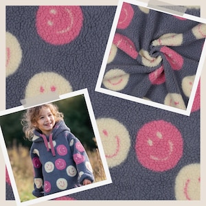 Könnte beinhalten: Blauer Kapuzenpullover mit einem Muster aus rosa und cremefarbenen Smiley-Gesichtern. Der Stoff hat eine strukturierte Optik. Das Bild zeigt auch eine Nahaufnahme des Stoffes.