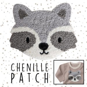 Könnte beinhalten: Ein Chenille-Patch in Form eines Waschbärgesichts mit grauen, weißen und schwarzen Details. Der Patch hat eine strukturierte Oberfläche und wird mit dem Text "CHENILLE PATCH" gezeigt. Ein kleines Bild zeigt den Patch auf einem langärmligen Oberteil.
