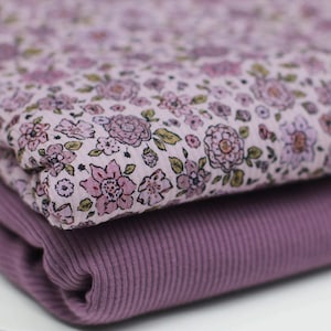 Peut inclure: Deux morceaux de tissu superposés. Le tissu supérieur est un imprimé floral avec des fleurs roses et des feuilles vertes sur un fond rose pâle. Le tissu inférieur est un tissu en tricot côtelé violet foncé uni. Parfait pour la couture.