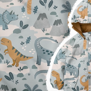 May include: A blue and brown children's jacket with a dinosaur print. The jacket features a variety of dinosaurs, including a triceratops, a stegosaurus, and a brachiosaurus. The dinosaurs are surrounded by green leaves and brown trees.