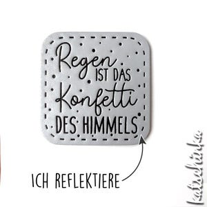 Könnte beinhalten: Ein silbernes Metallschild mit schwarzem Rand und dem Text "Regen ist das Konfetti des Himmels".