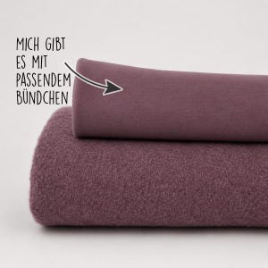 Könnte beinhalten: Zwei gefaltete Stoffstücke in einem gedeckten Mauveton. Das untere Stück hat eine dicke, flauschige, strukturierte Oberfläche, während das obere Stück ein glatter, flacher Strickstoff ist. Der Text im Bild lautet: MICH GIBT ES MIT PASSENDEM BÜNDCHEN.