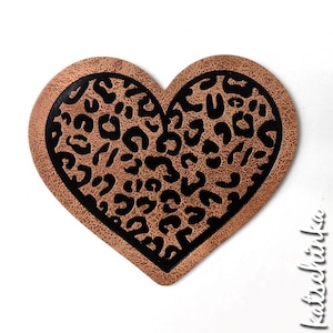 Puede incluir: Un parche de cuero marrón en forma de corazón con un diseño de estampado de leopardo negro.
