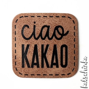 Könnte beinhalten: Ein braunes Leder-Patch mit einem genähten Rand. Der Text "ciao kakao" ist in Schwarz gedruckt.