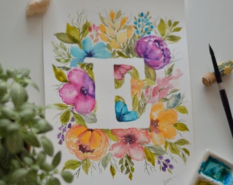 May include: Watercolour painting of the letter "E" surrounded by colourful flowers in shades of pink, orange, blue, and purple. A small blue butterfly is inside the letter. A paintbrush and watercolour palette are next to the painting. Floral art.