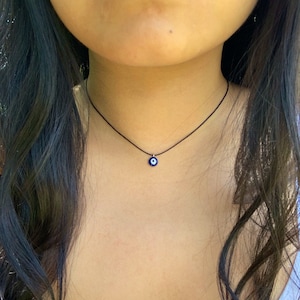 Pode incluir: Um colar choker preto simples com um pequeno pingente de olho azul.