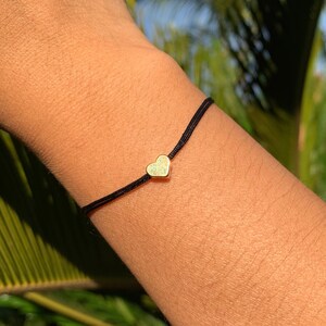 Puede incluir: Un sencillo brazalete de cuerda negra con un pequeño dije de corazón dorado.