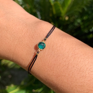 Op de afbeelding: Een eenvoudige zwarte armband met een enkel groen edelsteenbedeltje.
