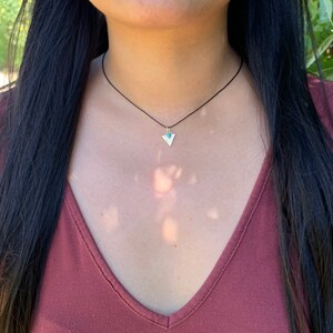 May include: A simple black cord necklace with a small silver triangle pendant featuring a turquoise stone.